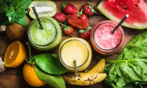 Tre colorati frullati di frutta con acqua, circondati da ingredienti freschi come fragole, kiwi, arance e spinaci.