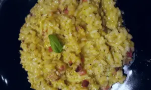 Un cremoso risotto basmati con zafferano, pancetta e una fogliolina di basilico, servito in un piatto nero.