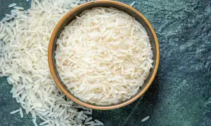 Chicchi di riso basmati in una ciotola e sparsi su una superficie scura. Il riso è noto per le sue proprietà nutritive e versatilità in cucina.