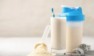 Un bicchiere di latte, una paletta con polvere proteica e uno shaker. Alcuni pensano che il siero del latte fa male, ma è un integratore comune.