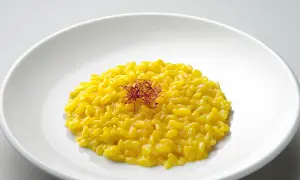 Un cremoso risotto giallo zafferano, guarnito con fili di zafferano, un piatto che promette un riso più leggero e gustoso.