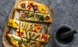 Focaccia di verdure colorata con cipolle rosse, pomodorini e erbe aromatiche, pronta per essere gustata.