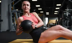 Donna esegue russian twist con palla medica in palestra, concentrata sull'allenamento addominale.