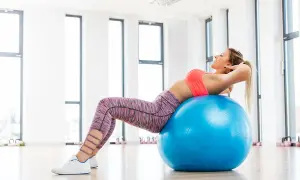 Donna sorridente esegue crunch su palla fitness, parte di esercizi con la palla per dimagrire.