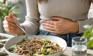 Donna con mano sulla pancia, forse il grano saraceno gonfia la pancia. Piatto di spaghetti integrali con verdure e un bicchiere d'acqua.