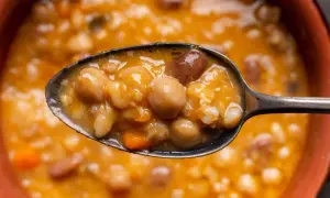 Un cucchiaio pieno di zuppa ricca di legumi e cereali, con ceci, fagioli e pezzetti di carota. Un piatto confortante e nutriente.