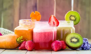 Tre vasetti di frullato di frutta colorati: arancione, rosa e verde. Fragole, kiwi e carote decorano i bicchieri.