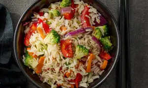 Un piatto colorato di riso con legumi e verdure miste: broccoli, peperoni rossi, carote e cipolla viola.