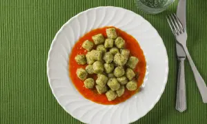 Gnocchi with broccoli in tomato sauce on a white plate, with a fork and knife.