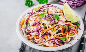 Insalate per dimagrire la pancia: cavolo cappuccio viola e bianco, carote grattugiate e coriandolo fresco, guarnite con spicchi di lime.