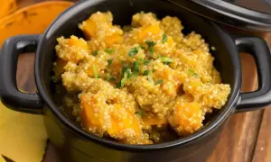 Un saporito piatto di quinoa e zucca, guarnito con erbe fresche, servito in una ciotola nera.