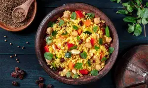 Un piatto colorato di cous cous, con ceci, verdure e uvetta, che evoca le sue antiche origini.