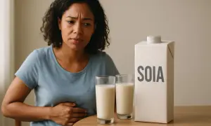 Donna con espressione sofferente tiene la mano sull'addome, accanto a un cartone di latte di soia e due bicchieri. Potrebbe essere un problema di colon irritabile.
