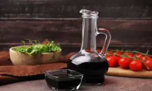 Aceto balsamico scuro in una caraffa di vetro e una ciotolina, con pomodorini e germogli sullo sfondo. Attenzione: l'aceto contiene nichel.