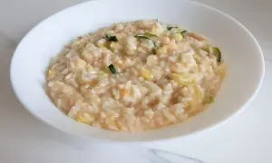 Un cremoso risotto con verdure light, arricchito da zucchine e altri ortaggi freschi, servito in una ciotola bianca.