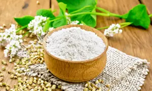 Farina di grano saraceno in ciotola, chicchi e fiori. Un alimento utile per chi soffre di colon irritabile.