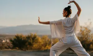 Donna pratica tai chi all'aperto, con le braccia sollevate e il corpo in posizione di equilibrio, immersa nella luce dorata del tramonto.