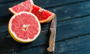 Mezzo pompelmo succoso e spicchi su un tavolo di legno scuro, pronti per essere gustati a stomaco vuoto.