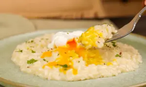 Un piatto di riso in bianco cremoso con un uovo in camicia dal tuorlo dorato che cola. Una forchettata di riso e uovo pronta per essere gustata.