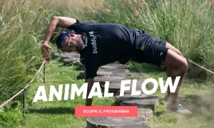 Uomo in posizione di animal flow, con il corpo arcuato e una mano a terra, immerso nella natura.