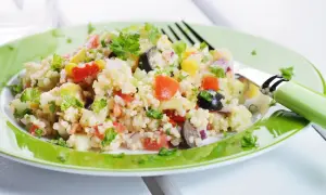 Un'insalata di miglio colorata con pomodori, olive, mais e prezzemolo fresco, servita su un piatto verde brillante.