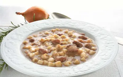 Piatto di pasta e fagioli borlotti, con cipolla e rosmarino sullo sfondo. Un comfort food che scalda il cuore.