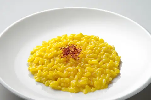 Un cremoso risotto giallo zafferano, guarnito con fili di zafferano, un piatto che promette un riso più leggero e gustoso.