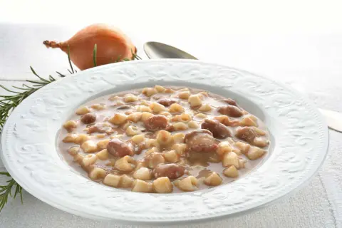 Piatto di pasta e fagioli borlotti, con cipolla e rosmarino sullo sfondo. Un comfort food che scalda il cuore.