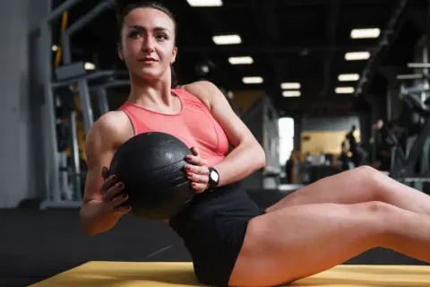 Donna esegue russian twist con palla medica in palestra, concentrata sull'allenamento addominale.