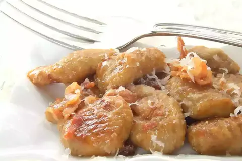 Gnocchi e lenticchie dorati, conditi con formaggio grattugiato e un tocco di pancetta croccante.