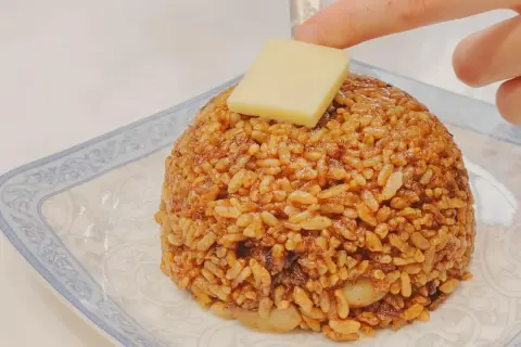 Un monticello di riso con salsa di soia e uova, guarnito con un cubetto di formaggio.