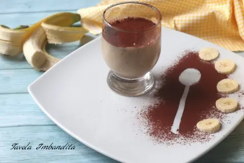 Delizioso dessert al bicchiere con banana e cacao amaro, guarnito con fettine di banana e una spolverata di cacao.