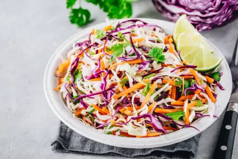 Insalate per dimagrire la pancia: cavolo cappuccio viola e bianco, carote grattugiate e coriandolo fresco, guarnite con spicchi di lime.