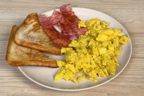 Piatto con uova strapazzate, bacon croccante e pane tostato. Un classico per iniziare la giornata con gusto.