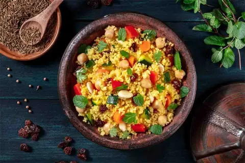 Un piatto colorato di cous cous, con ceci, verdure e uvetta, che evoca le sue antiche origini.
