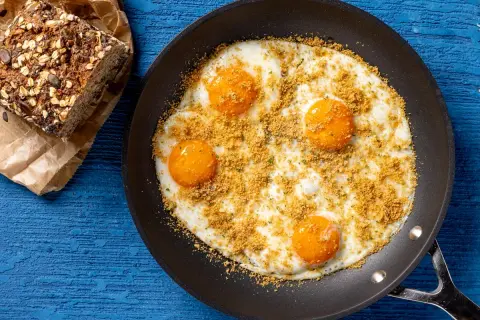 Uova fritte in padella con pangrattato e erbe, accompagnate da pane integrale. Un'idea per ricette fit con uova, sana e gustosa.
