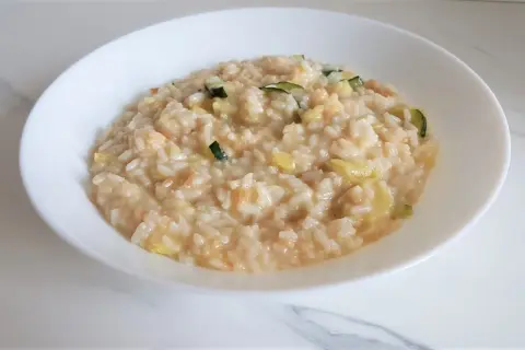 Un cremoso risotto con verdure light, arricchito da zucchine e altri ortaggi freschi, servito in una ciotola bianca.