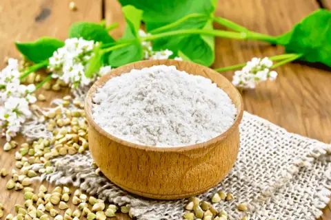 Farina di grano saraceno in ciotola, chicchi e fiori. Un alimento utile per chi soffre di colon irritabile.