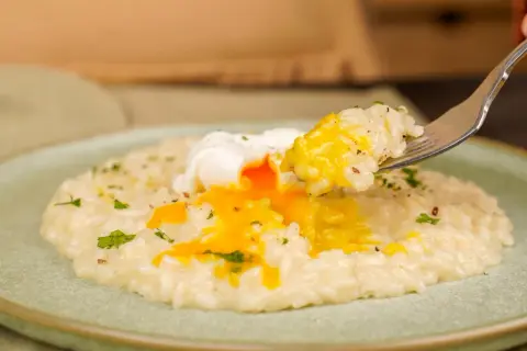 Un piatto di riso in bianco cremoso con un uovo in camicia dal tuorlo dorato che cola. Una forchettata di riso e uovo pronta per essere gustata.