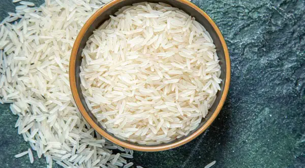 Chicchi di riso basmati in una ciotola e sparsi su una superficie scura. Il riso è noto per le sue proprietà nutritive e versatilità in cucina.