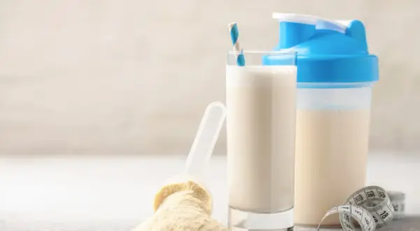 Un bicchiere di latte, una paletta con polvere proteica e uno shaker. Alcuni pensano che il siero del latte fa male, ma è un integratore comune.