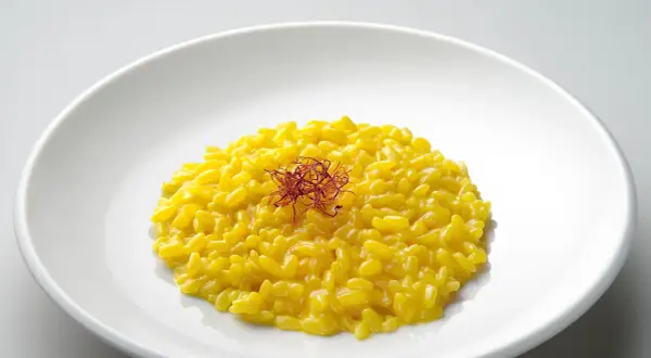 Un cremoso risotto giallo zafferano, guarnito con fili di zafferano, un piatto che promette un riso più leggero e gustoso.