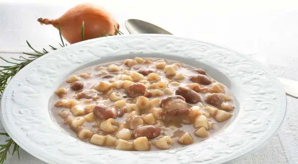Piatto di pasta e fagioli borlotti, con cipolla e rosmarino sullo sfondo. Un comfort food che scalda il cuore.