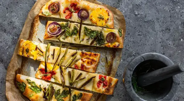 Focaccia di verdure colorata con cipolle rosse, pomodorini e erbe aromatiche, pronta per essere gustata.