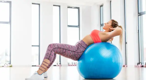 Donna sorridente esegue crunch su palla fitness, parte di esercizi con la palla per dimagrire.