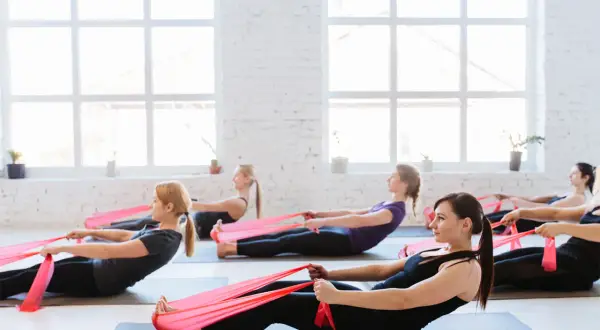 Donne in posa pilates con elastici rossi, un allenamento efficace per chi vuole che il pilates fa dimagrire.