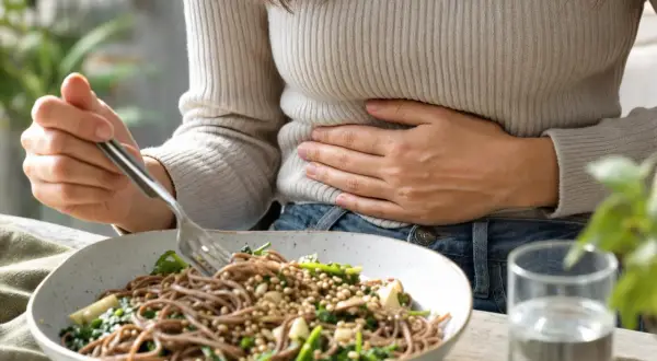 Donna con mano sulla pancia, forse il grano saraceno gonfia la pancia. Piatto di spaghetti integrali con verdure e un bicchiere d'acqua.