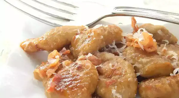 Gnocchi e lenticchie dorati, conditi con formaggio grattugiato e un tocco di pancetta croccante.
