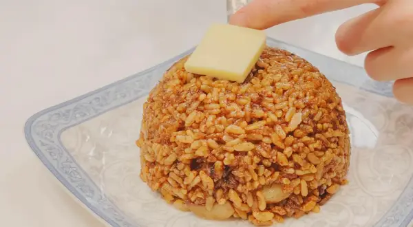 Un monticello di riso con salsa di soia e uova, guarnito con un cubetto di formaggio.