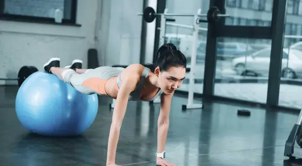 Donna esegue addominali con la palla, mantenendo la posizione plank con i piedi appoggiati sulla palla svizzera blu.